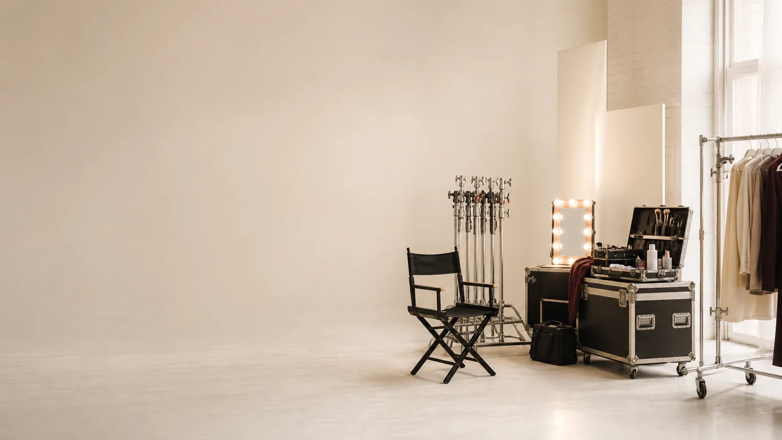 Make-up station with an illuminated mirror, director chair, light stands and a wardrobe rail in a bright studio
